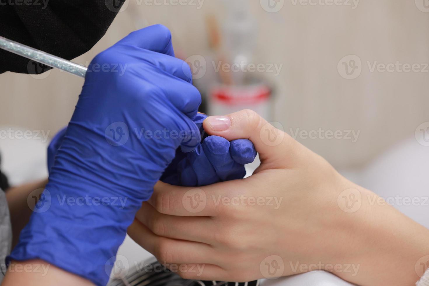 Closeup shot of manicure in a beauty salon. Master during a manicure. Master manicurist varnishes the gel on the nails of a female client. The concept of beauty and health. photo