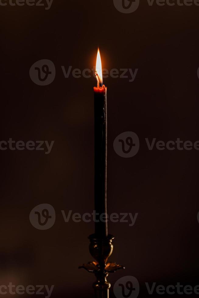 one candle burning at night on the black background in church. Candle isolated in black background. Close-up. selective focus photo