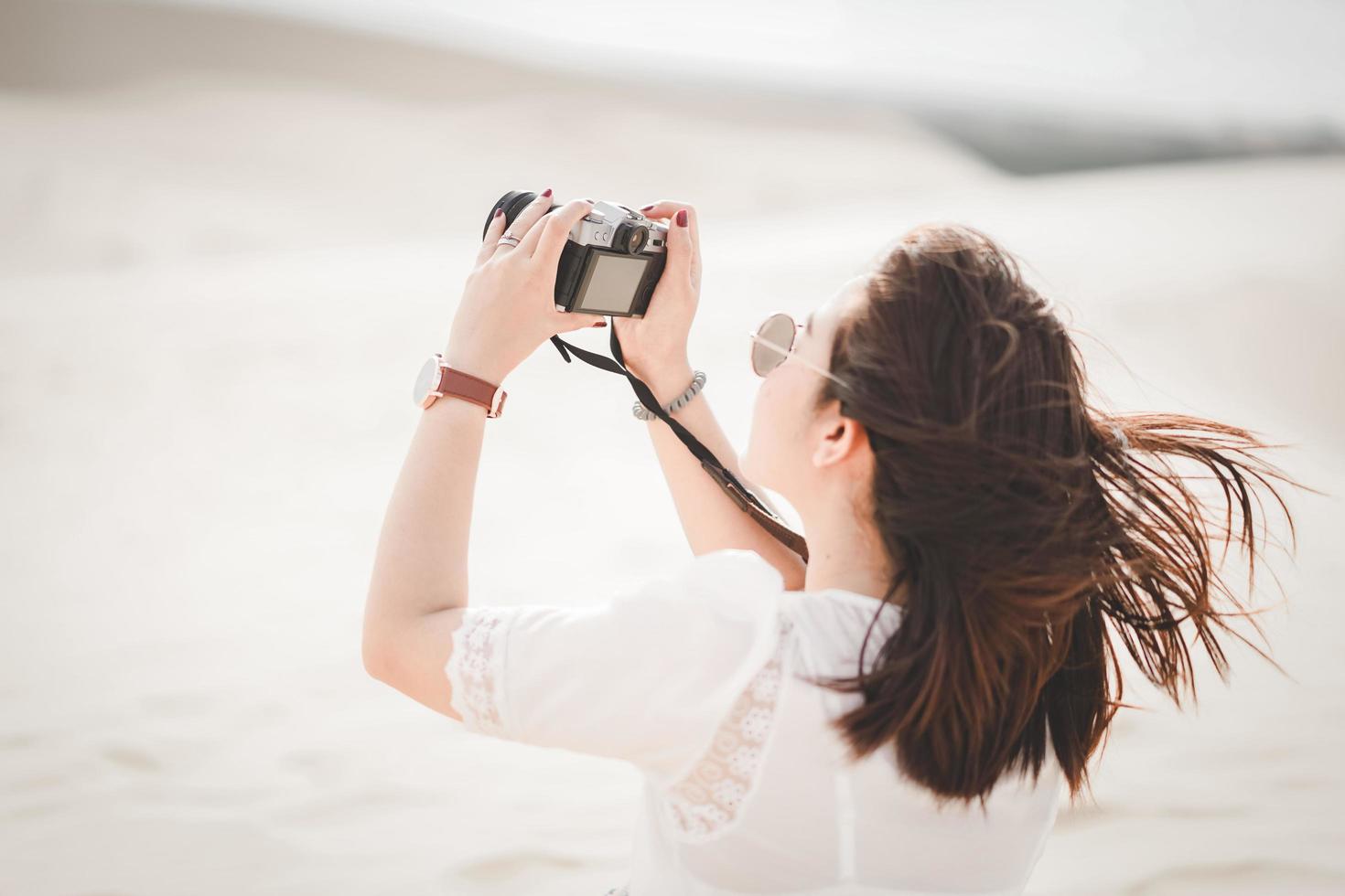 Traveling and photography. Young woman with camera taking photo at White Sand Dunes, Vietnam