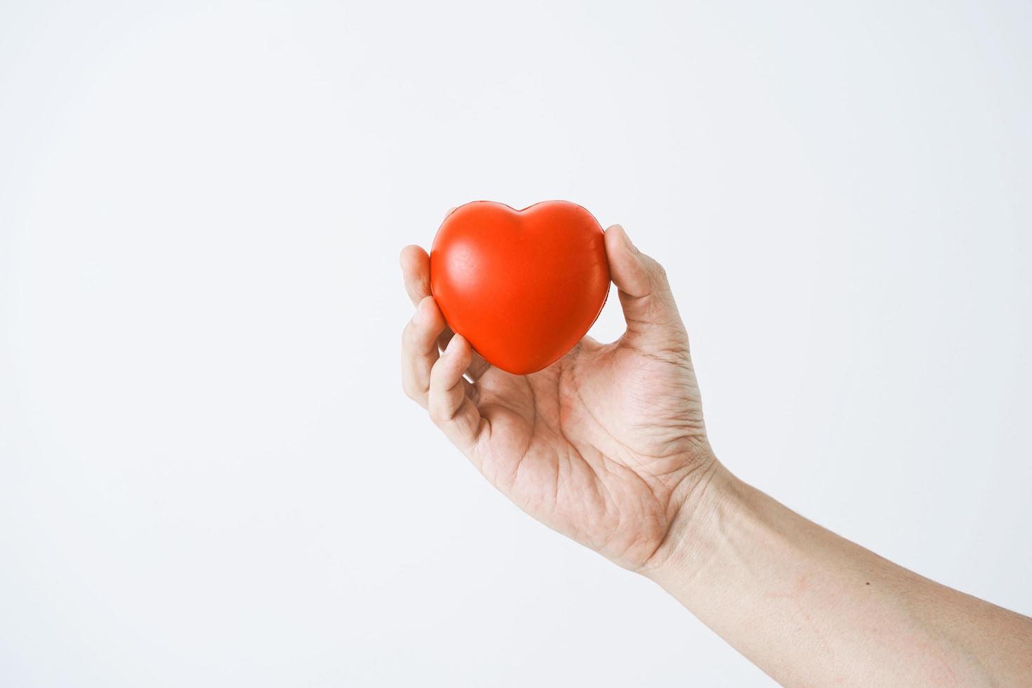La mano de un hombre que sostiene un corazón rojo sobre fondo blanco. foto