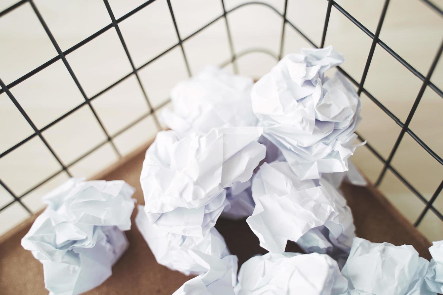 cesto de basura y arrugas de papel. desbordamiento de papel usado en la papelera de la oficina. de cerca foto