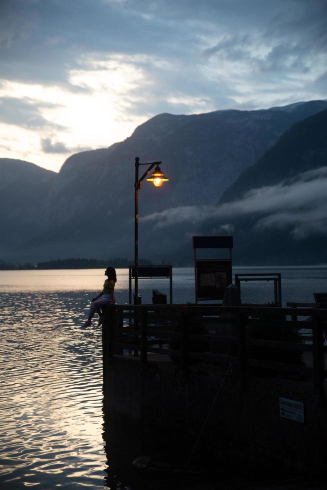 Mujer en el antiguo muelle de madera mirando la puesta de sol sobre el lago del mar de Hallstatt foto