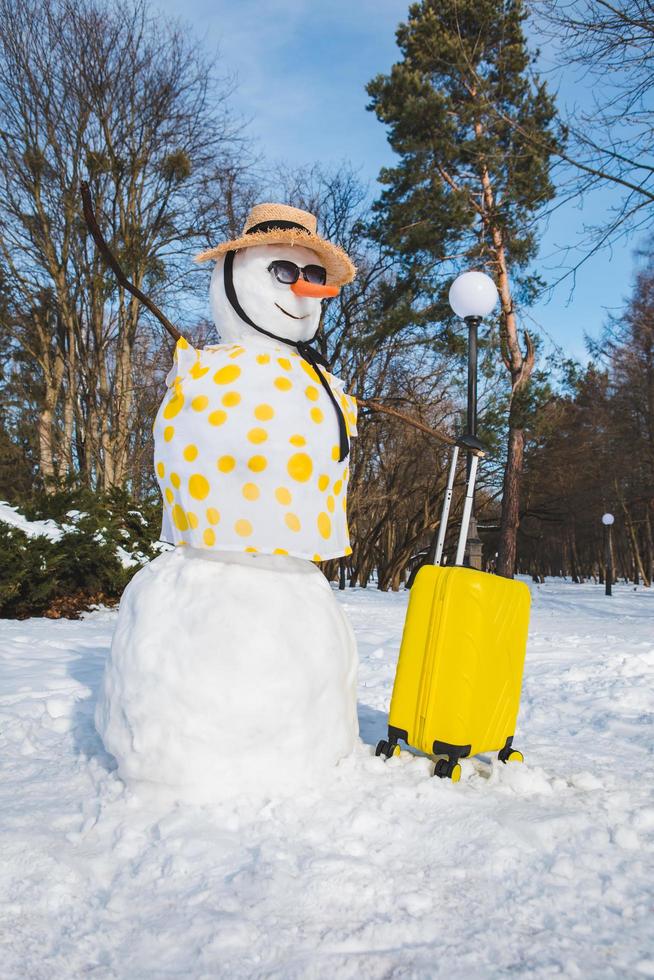 Snowman with valise ready for travel to tropical country photo