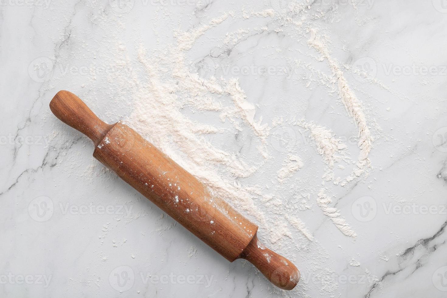 Scattered wheat flour and rolling pin set up on white marble background flat lay. photo