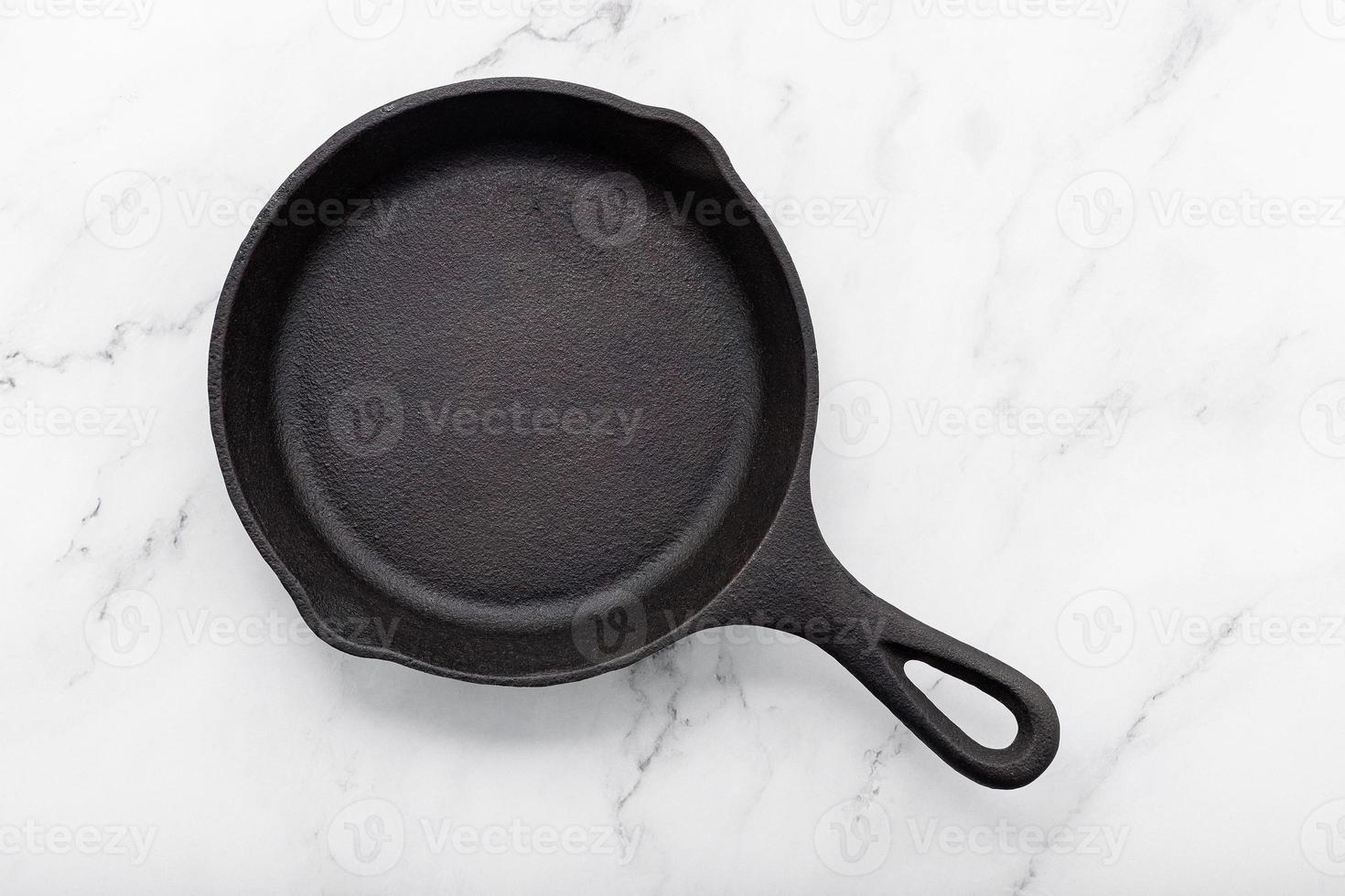 Empty old cast iron skillet set up on white marble  background with flat lay and copy space. photo