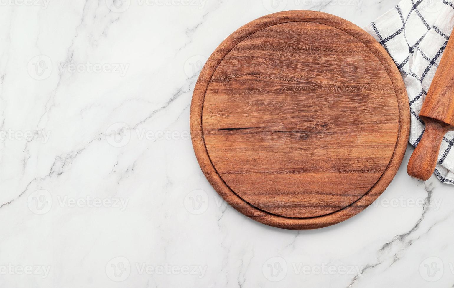 Plato de pizza de madera vacía con servilleta y rodillo sobre la mesa de la cocina de piedra de mármol. Tablero de pizza y mantel sobre fondo de mármol blanco. foto