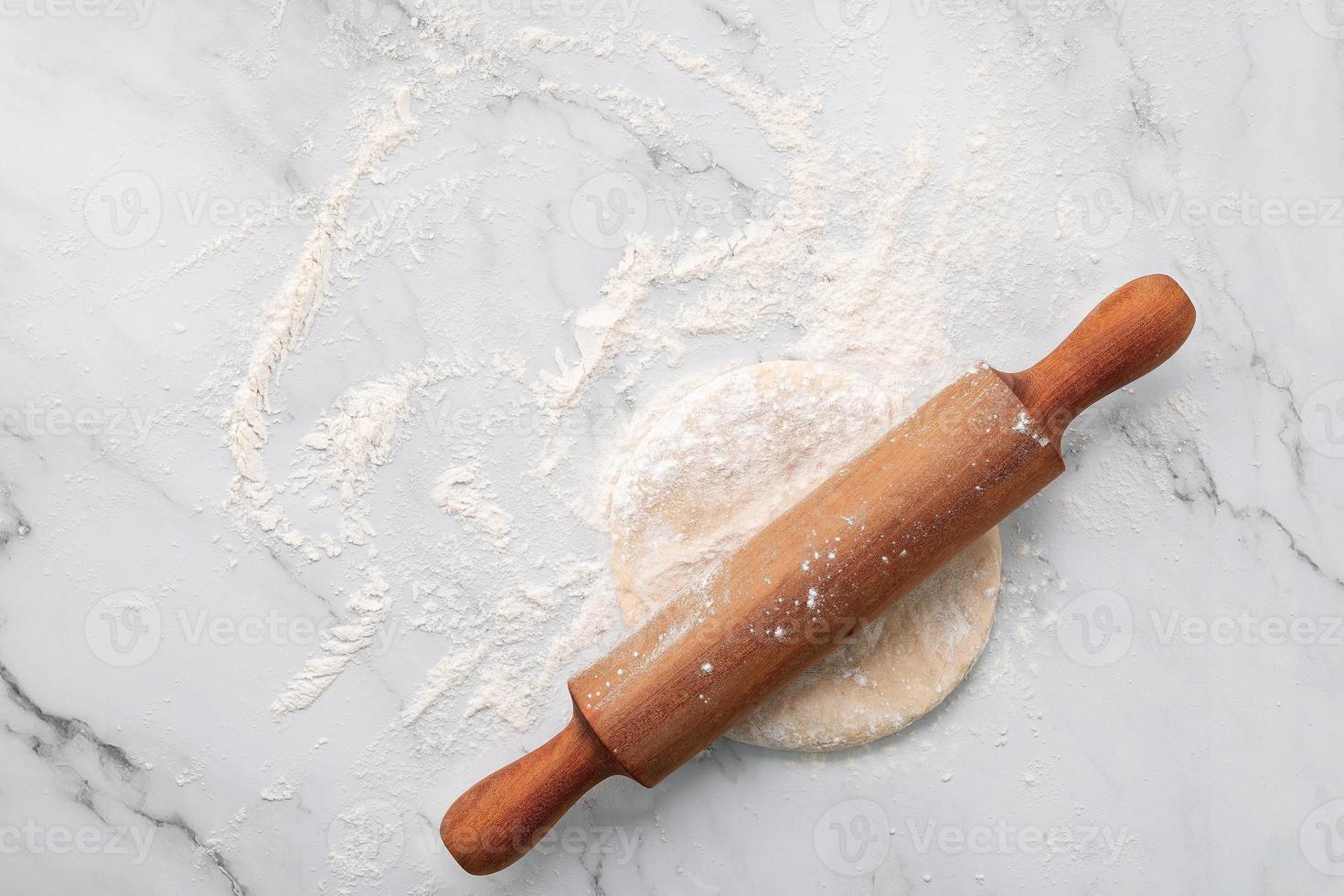 Scattered wheat flour and fresh homemade yeast dough kneaded on marble table with rolling pin on marble table flat lay. photo