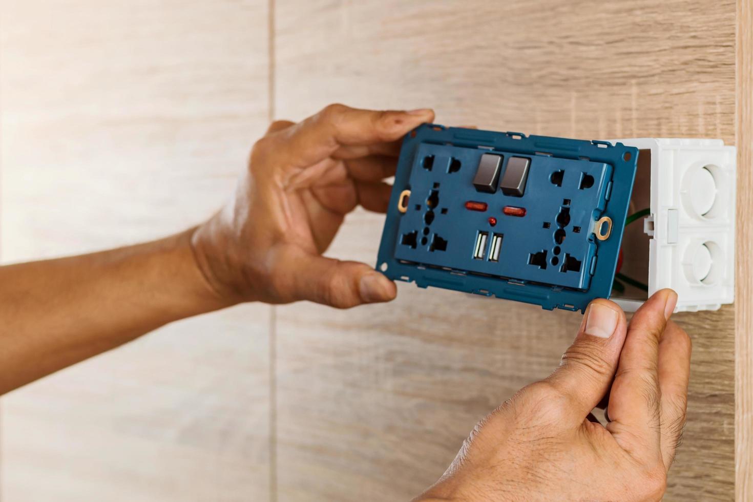 La mano de un electricista está instalando el enchufe de alimentación de CA del tomacorriente de pared universal con puerto USB y encendido-apagado en una caja de plástico en una pared de madera. foto