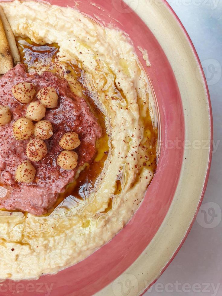 Hummus, arabic chickpea dip, with spices in a pink cream plate. Top view abstract capture. Copy space photo