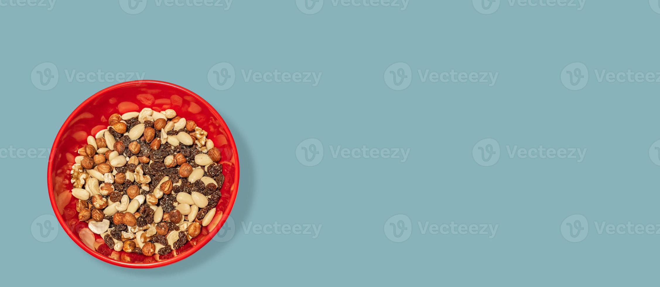 Banner with different nuts and raisin collected at red plastic plate at turquoise green blue background with copy space, closeup, details. Concept healthy diet and nutritious food. photo