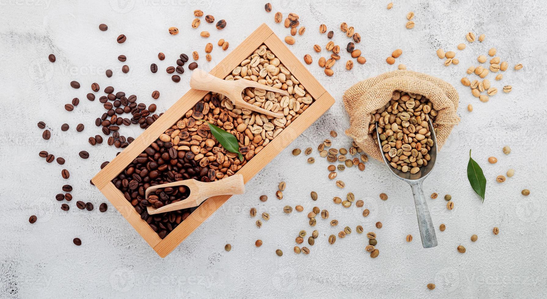 Café descafeinado verde y marrón sin tostar y granos de café tostados oscuros en caja de madera con configuración de cucharadas sobre fondo de hormigón blanco. foto