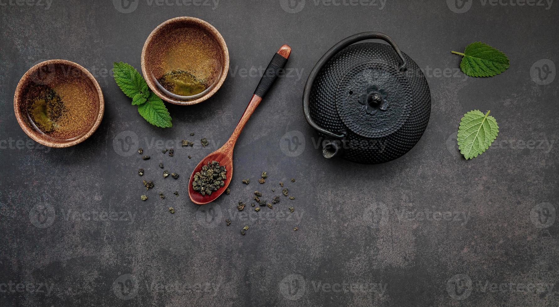 Black cast iron tea pot with herbal tea set up on dark stone background. photo