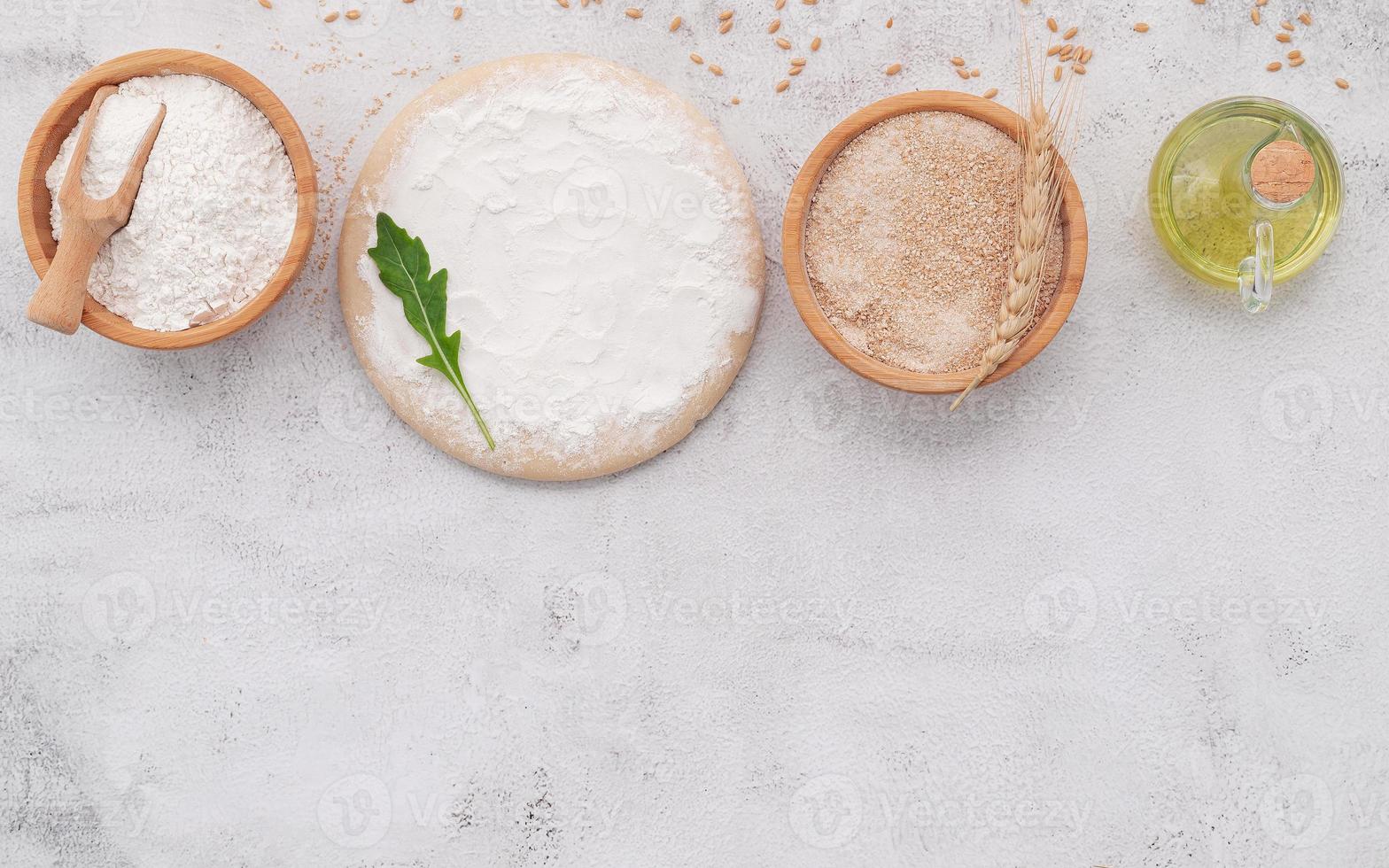 The ingredients for homemade pizza dough with wheat ears ,wheat flour and wheat grains set up on white concrete background. photo
