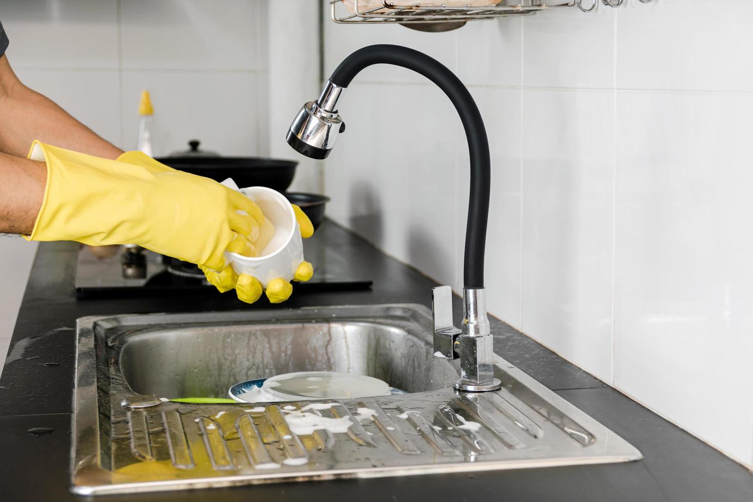 Human hands in yellow rubber gloves washing a ceramic coffee mug in the kitchen sink. photo