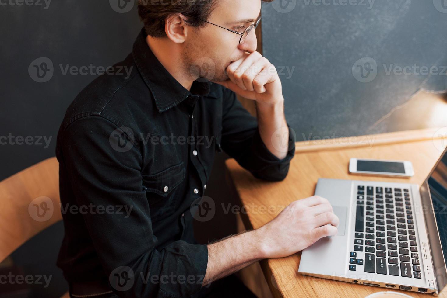 Diseñador de hombre creativo trabajando en su computadora portátil mientras espera pedidos en su café favorito en el interior, estudiante trabajando en net-book durante el desayuno de la mañana en el interior de la cafetería moderna foto