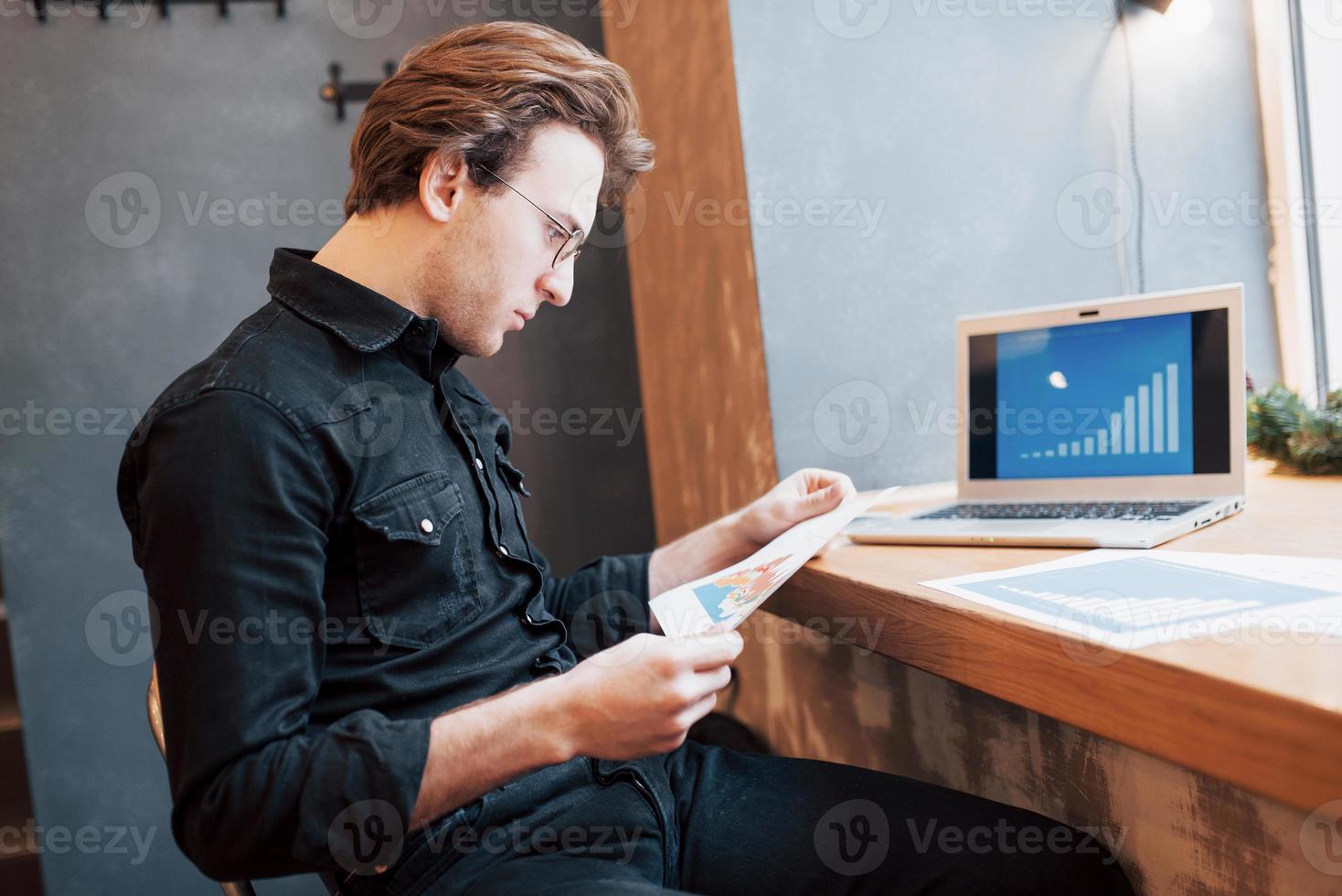 Businessman using laptop with tablet and pen on wooden table in coffee shop with a cup of coffee. An entrepreneur who manages his company remotely as a freelancer. photo