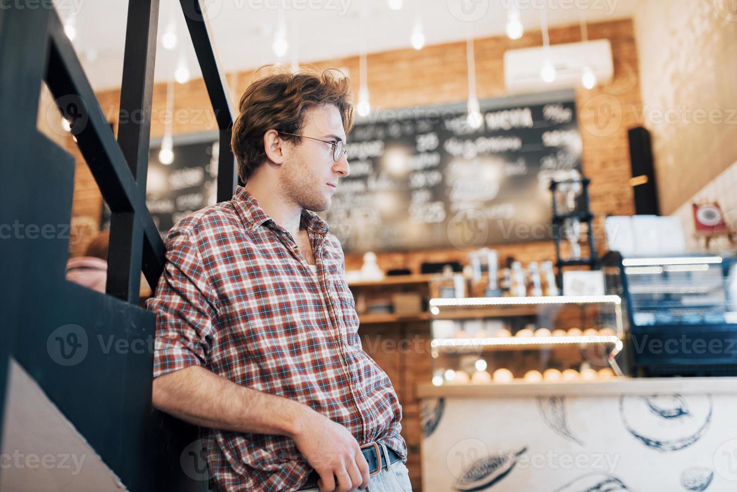 Thoughtful young man is sitting in confectionery shop. She is drinking coffee while waiting for someone photo