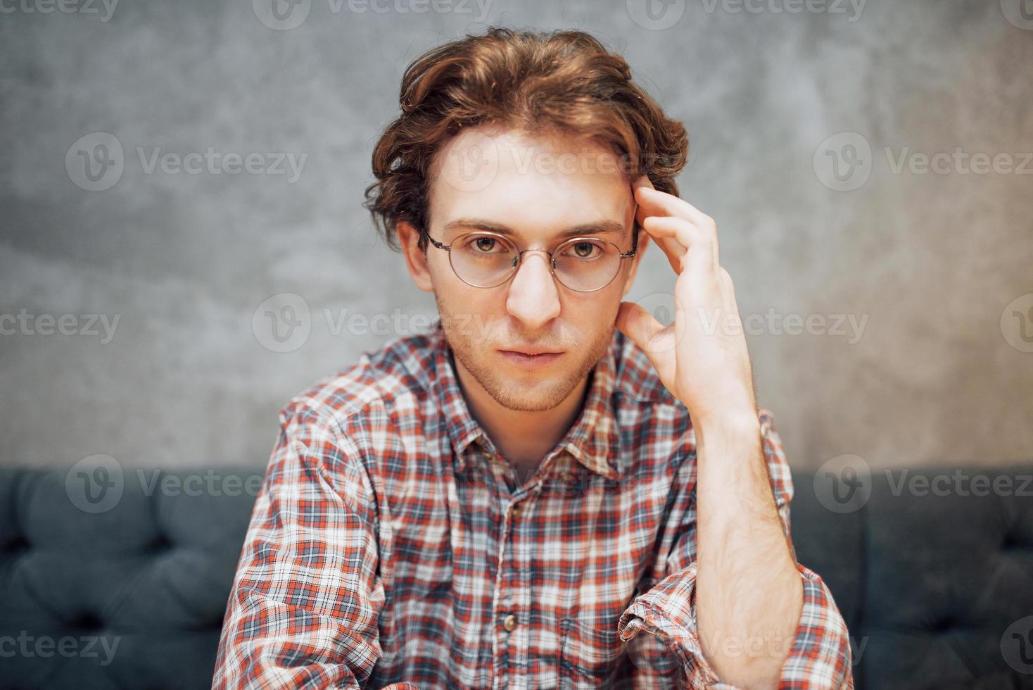 Retrato de hombre guapo y relajado sentado en un café y pensando, trabajando a distancia, mirando a la cámara foto