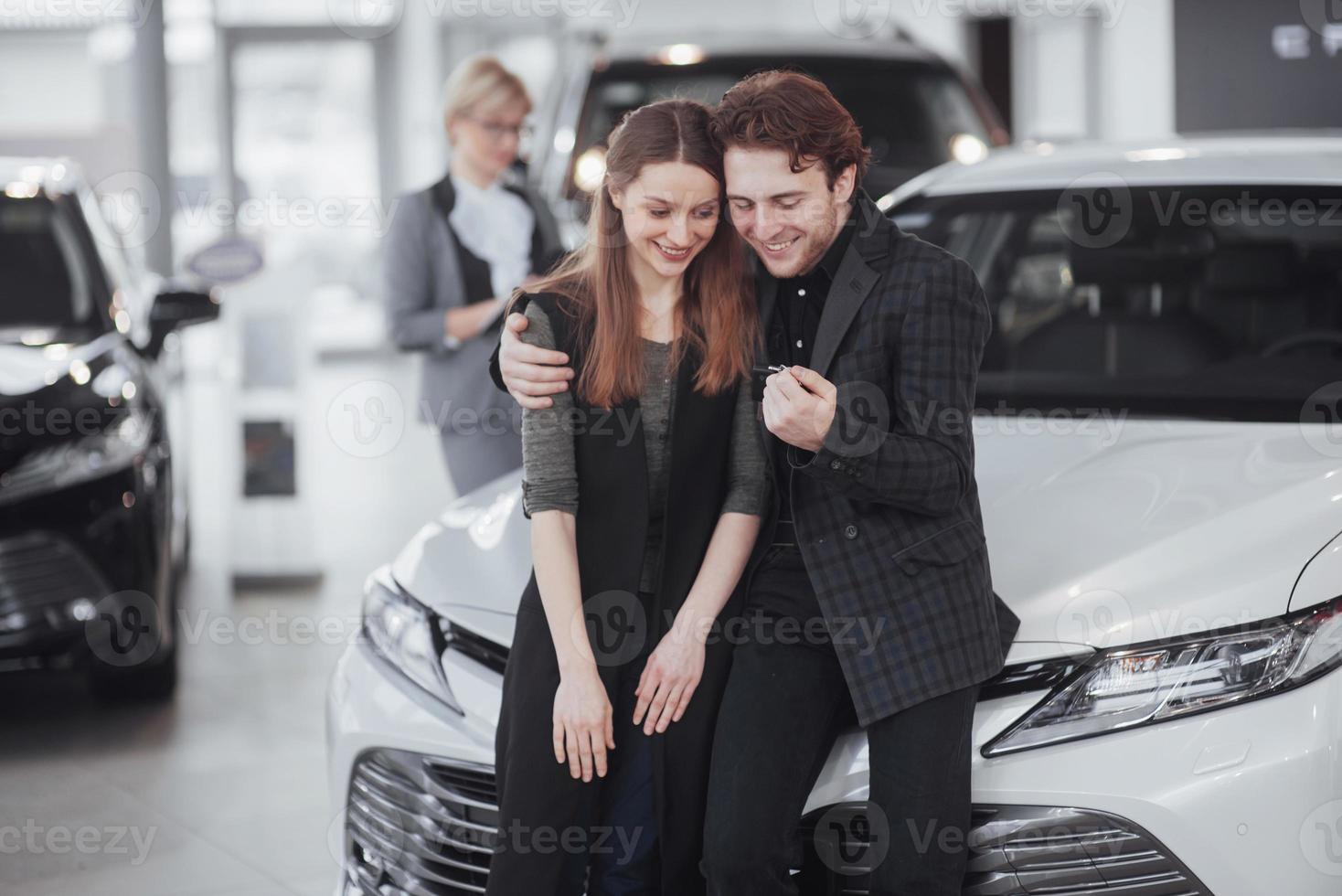 ahora su sueño se hace realidad. vendedor de coches dando la llave del coche nuevo a los jóvenes propietarios atractivos foto