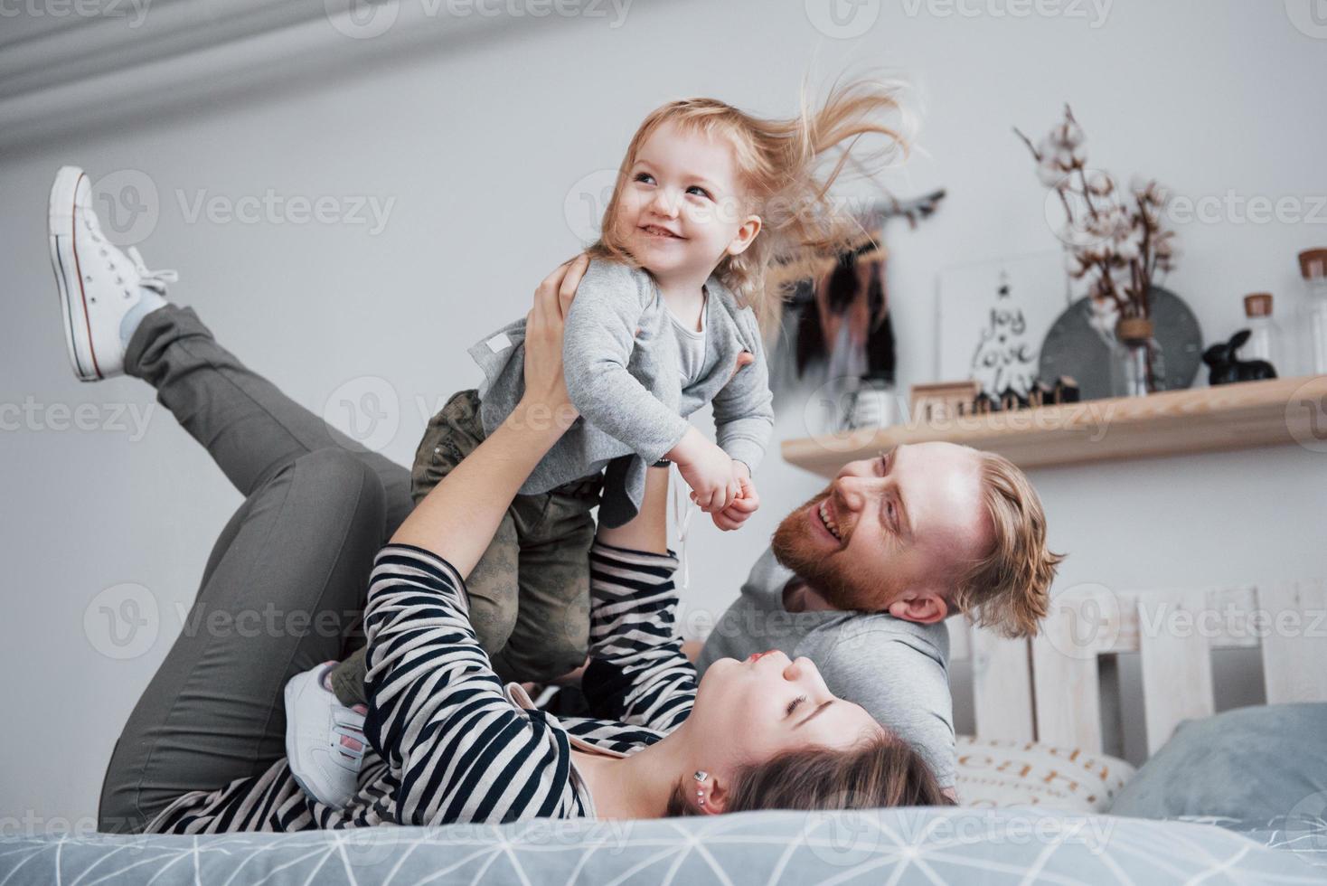 feliz madre de familia, padre e hija niño se ríe en la cama foto