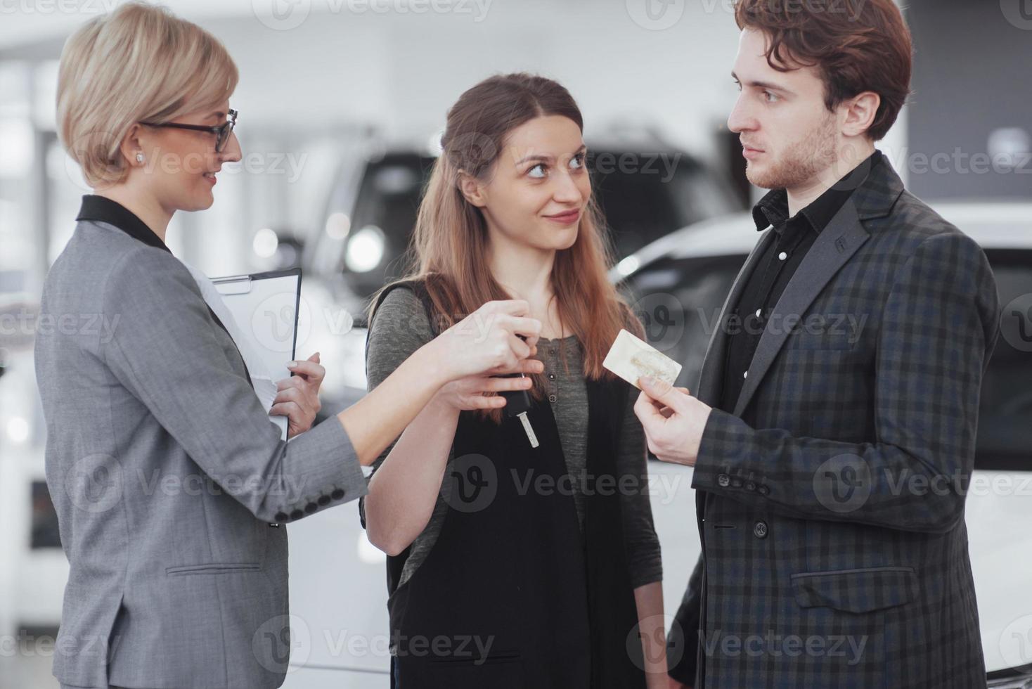 listo para montar. Hermosa pareja amorosa posando juntos cerca de su auto nuevo en el salón de exposición del concesionario de autos sonriendo felizmente mostrando las llaves de su auto transporte alquiler de vehículos comprando bienestar estilo de vida foto