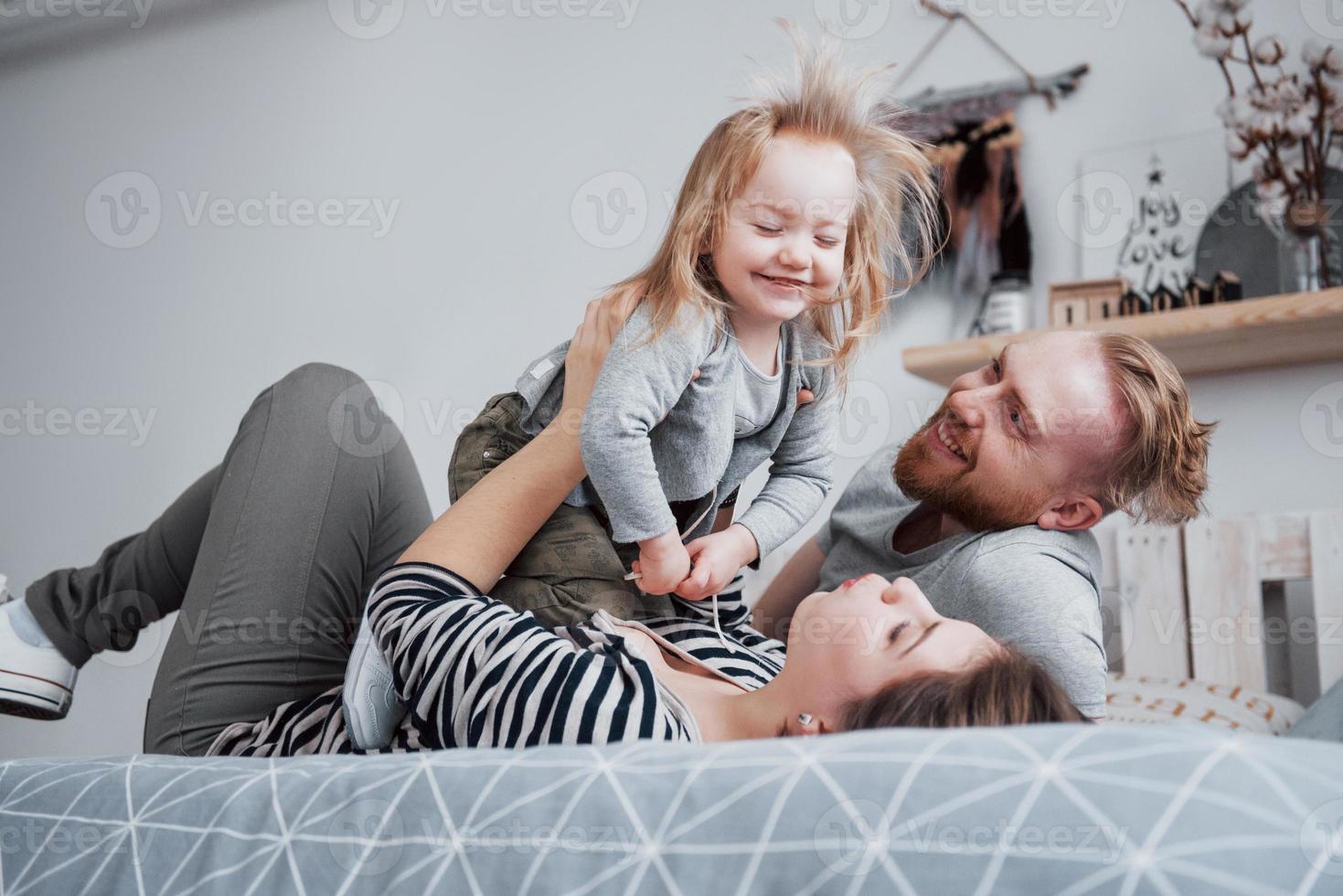 feliz madre de familia, padre e hija niño se ríe en la cama foto