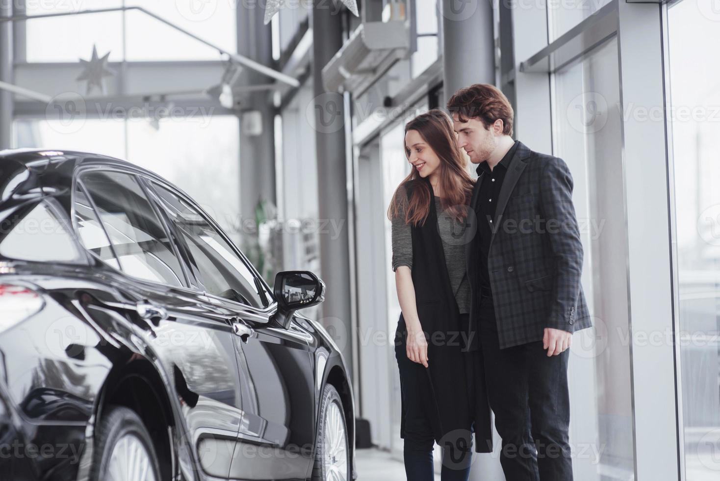 es el único coche que quiero. Hermosa joven pareja de pie en el concesionario eligiendo el coche para comprar foto