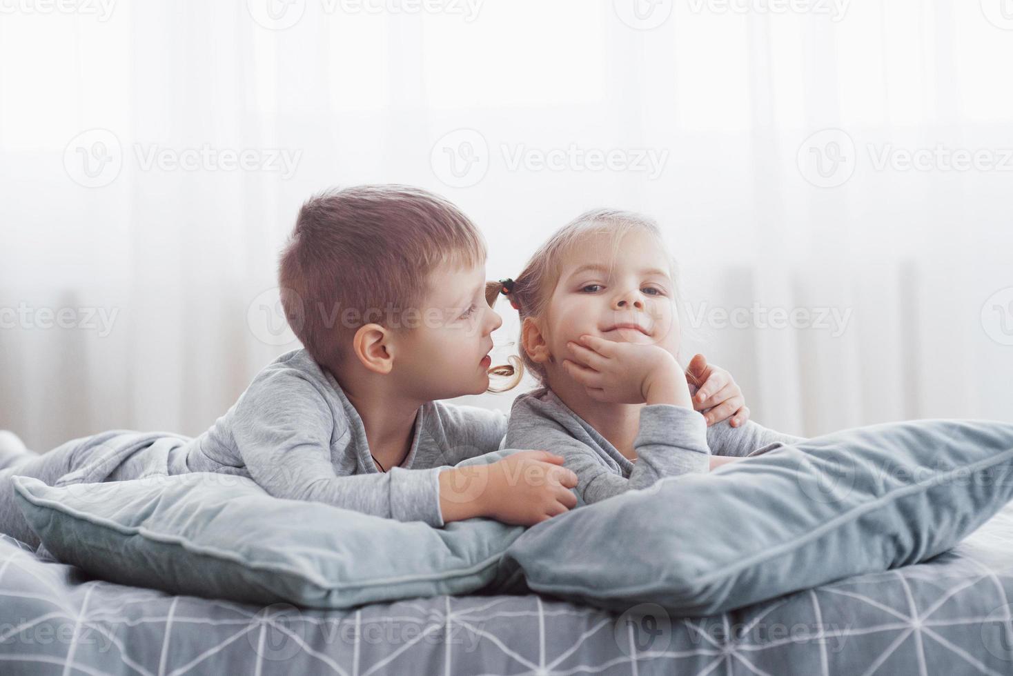 Kids playing in parents bed. Children wake up in sunny white bedroom. Boy and girl play in matching pajamas. Sleepwear and bedding for child and baby. Nursery interior for toddler kid. Family morning photo