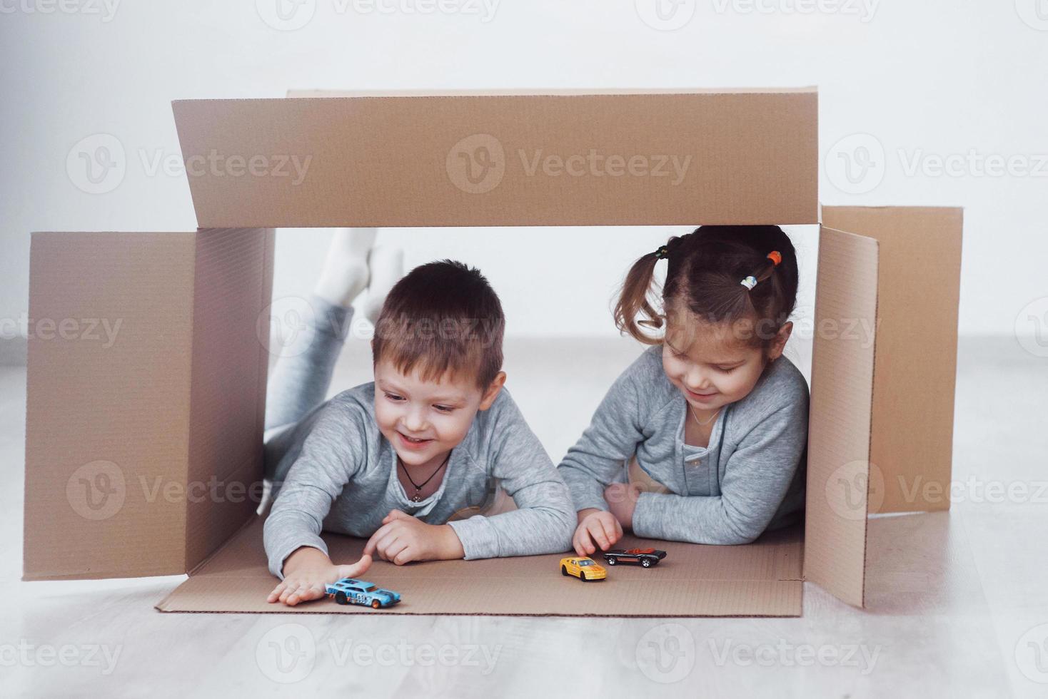 dos niños pequeños niño y niña jugando autos pequeños en cajas de cartón. foto de concepto. los niños se divierten. foto de concepto. los niños se divierten