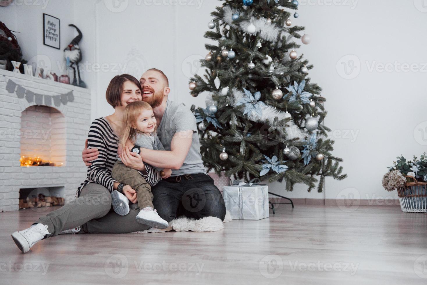 feliz navidad y próspero año nuevo hermosa mamá, papá e hija están usando una computadora portátil y sonriendo mientras están sentados cerca de los regalos de navidad foto