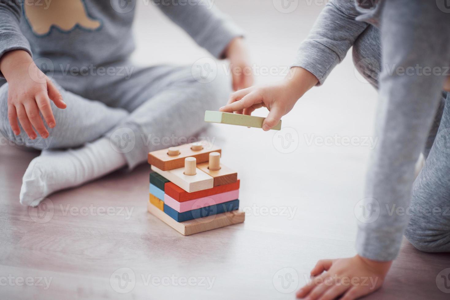 Los niños juegan con un diseñador de juguetes en el piso de la habitación de los niños. dos niños jugando con bloques de colores. juegos educativos de jardín de infantes foto