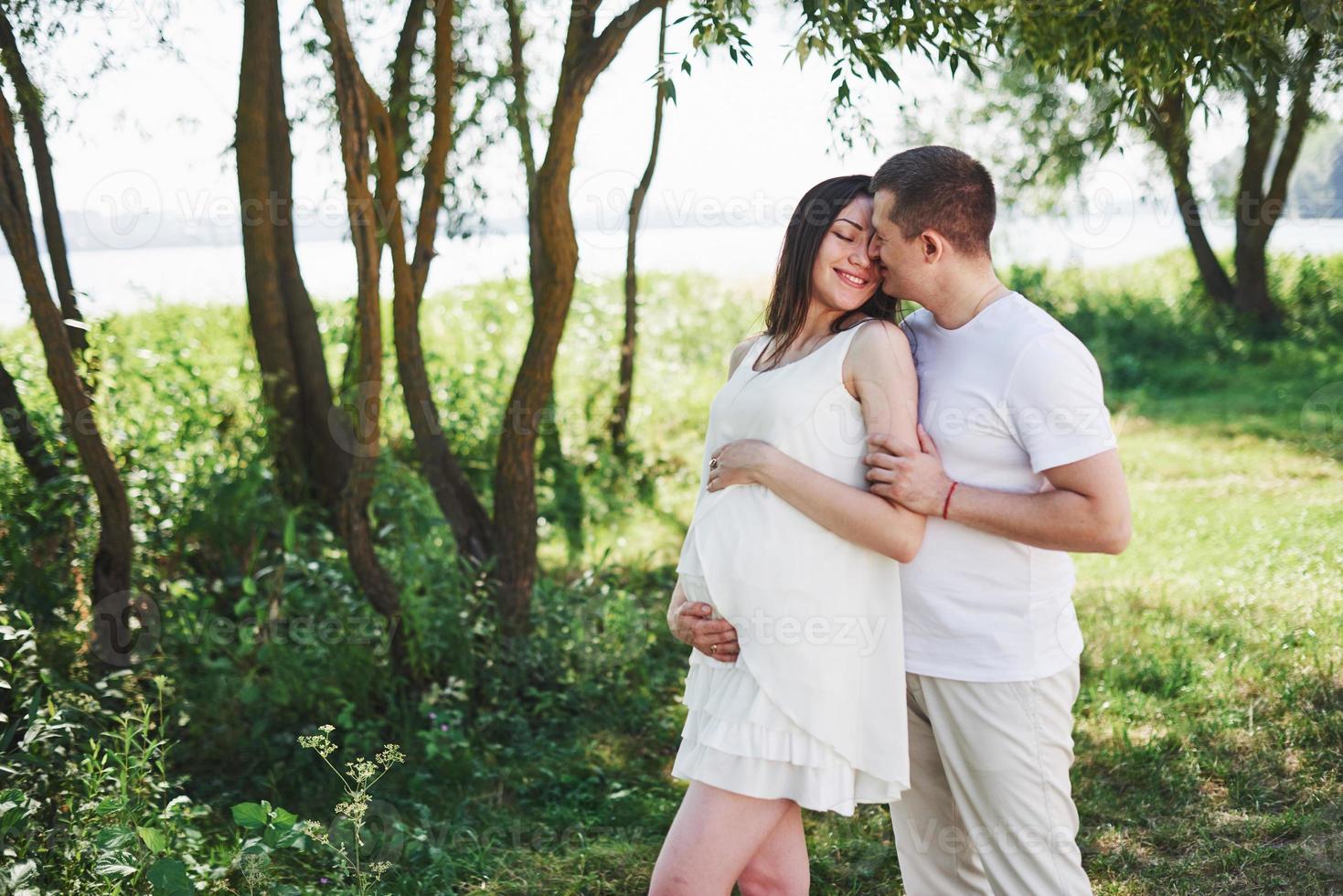 Feliz y joven pareja embarazada abrazándose en la naturaleza foto