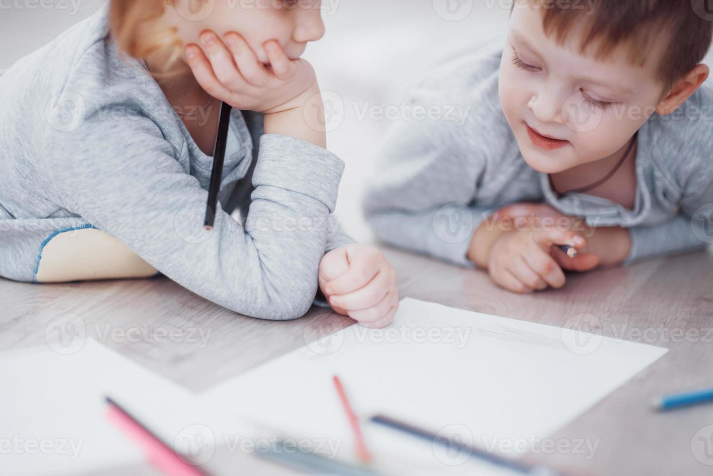 Children lie on the floor in pajamas and draw with pencils. Cute child painting by pencils.Hand of child girl and boy draw and paint with crayon. Close up view photo