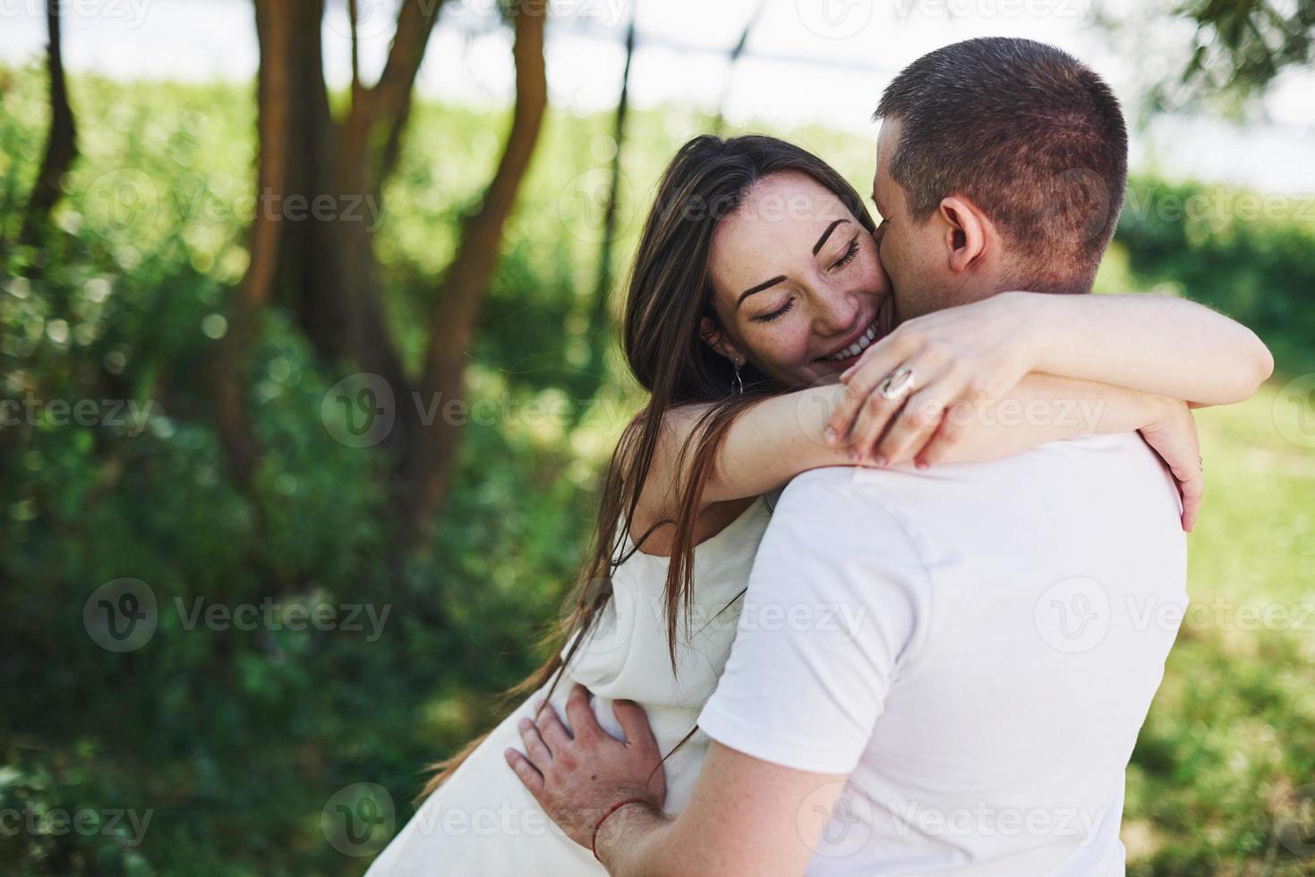 feliz y joven pareja embarazada abrazándose en la naturaleza. momentos romanticos foto