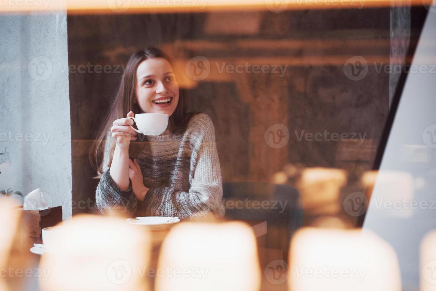 Hermosa joven disfrutando de café capuchino con espuma cerca de la ventana en un café foto