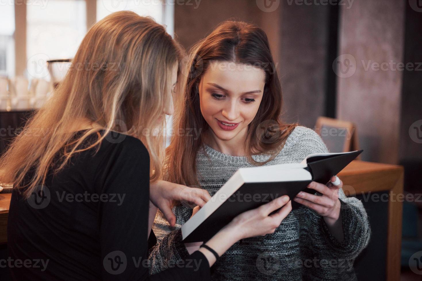 dos niñas absortas en la lectura de libros durante el descanso en el café. lindas y encantadoras mujeres jóvenes están leyendo un libro y bebiendo café foto