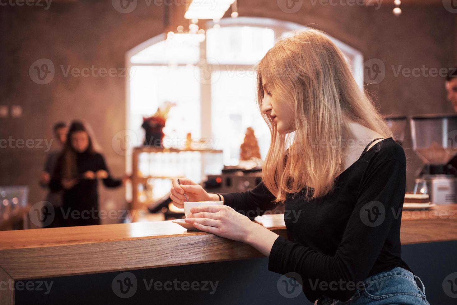 Mujer sonriente en la cafetería mediante teléfono móvil y mensajes de texto en las redes sociales, sentada sola foto