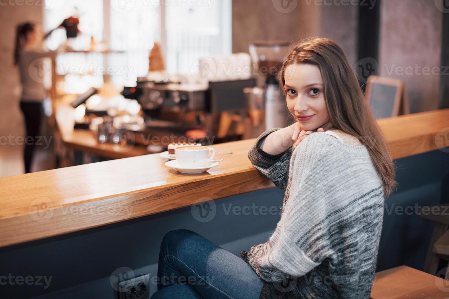 Mujer sonriente en la cafetería mediante teléfono móvil y mensajes de texto en las redes sociales, sentada sola foto