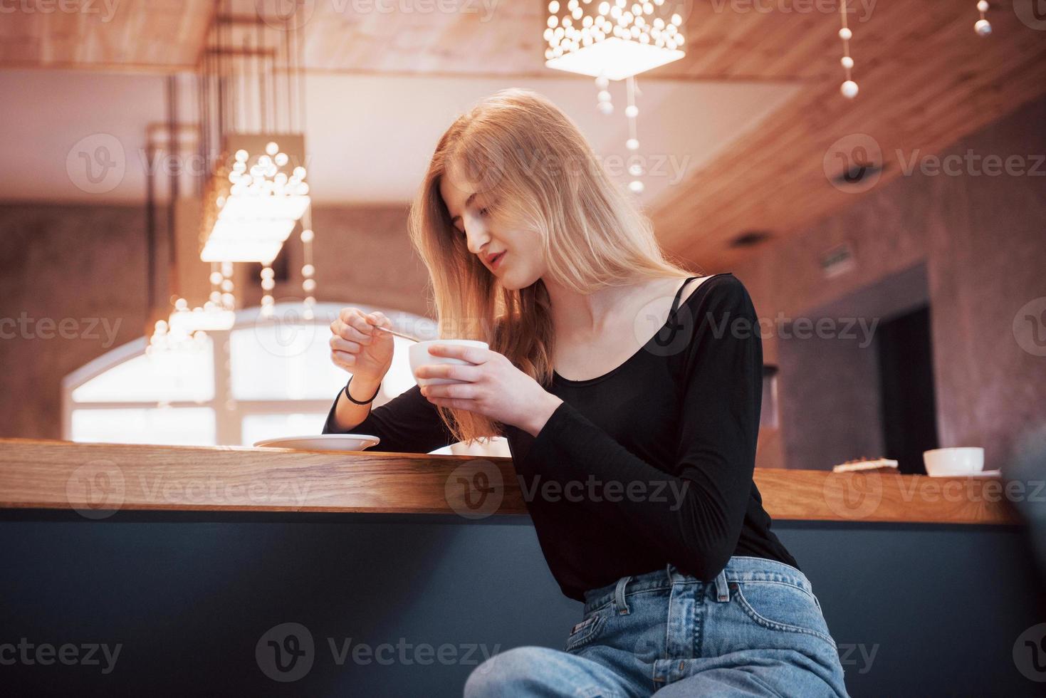 Mujer sonriente en la cafetería mediante teléfono móvil y mensajes de texto en las redes sociales, sentada sola foto