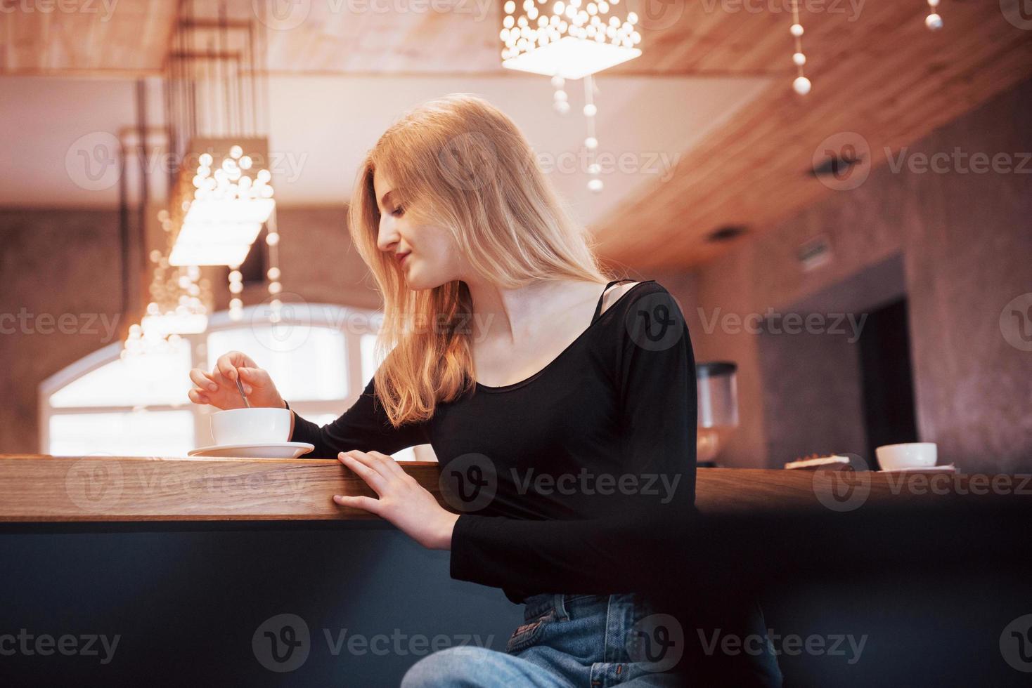 Mujer sonriente en la cafetería mediante teléfono móvil y mensajes de texto en las redes sociales, sentada sola foto