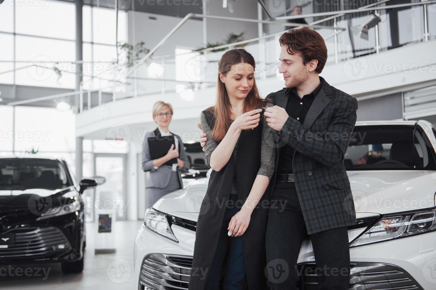 es el único coche que quiero. Hermosa joven pareja de pie en el concesionario eligiendo el coche para comprar foto