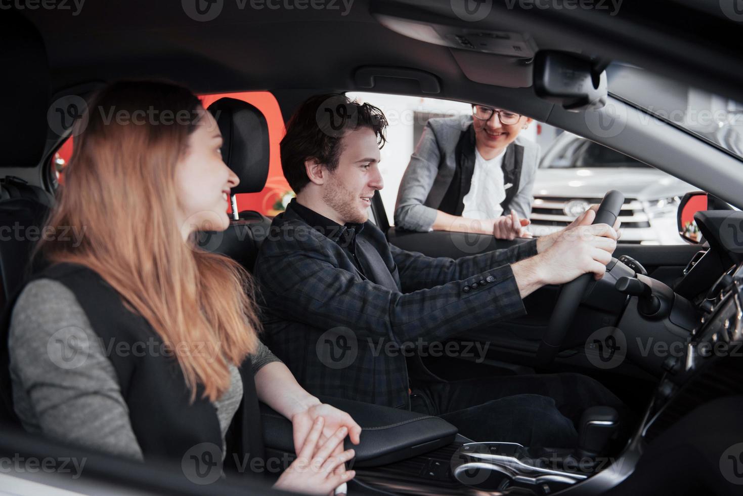 Check put the stereo system. Handsome mature man smiling at his wife turning on music while sitting in their new car together photo