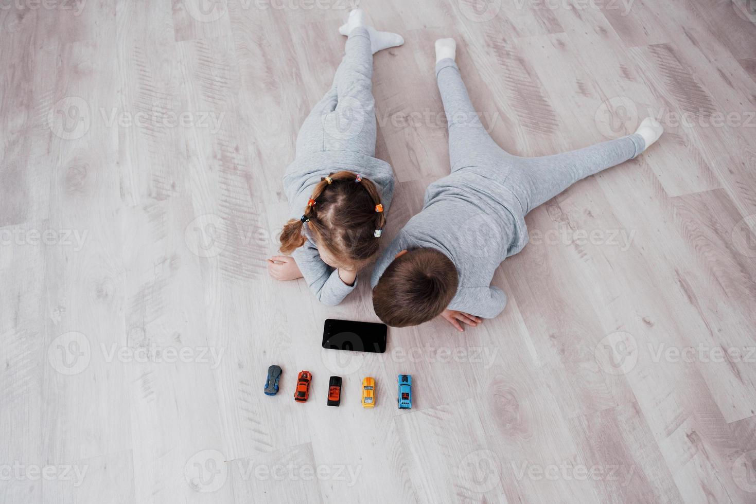 Top view. Children using digital gadgets at home. Brother and sister on pajamas watch cartoons and play games on their technology tablet photo