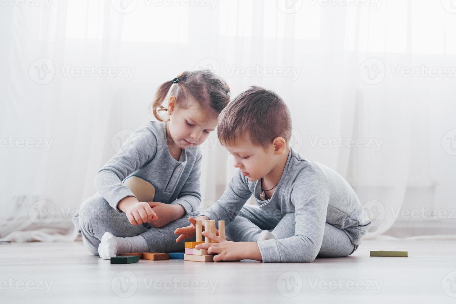 Los niños juegan con un diseñador de juguetes en el piso de la habitación de los niños. dos niños jugando con bloques de colores. juegos educativos de jardín de infantes foto