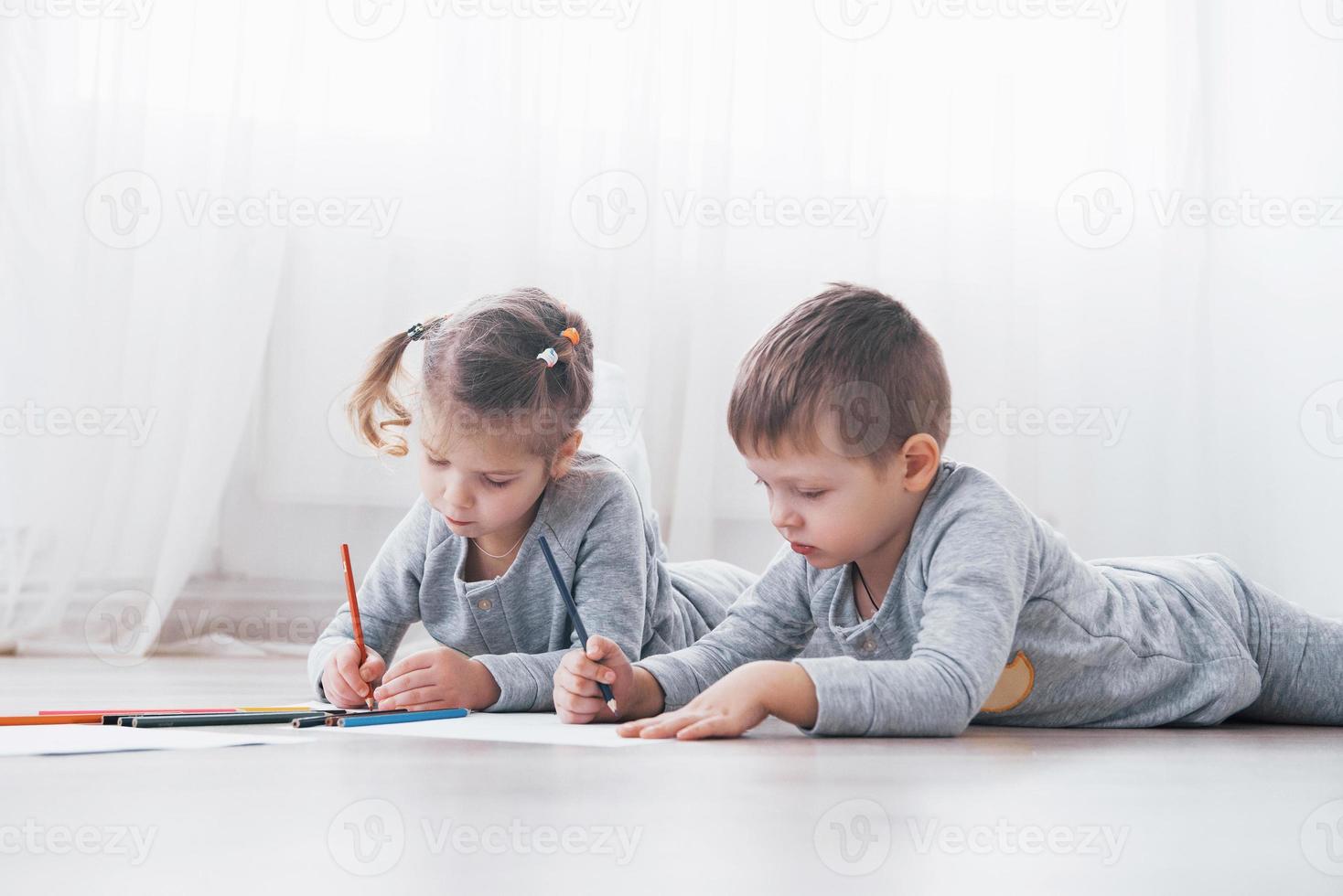 los niños se acuestan en el suelo en pijama y dibujan con lápices. lindo niño pintando con lápices foto