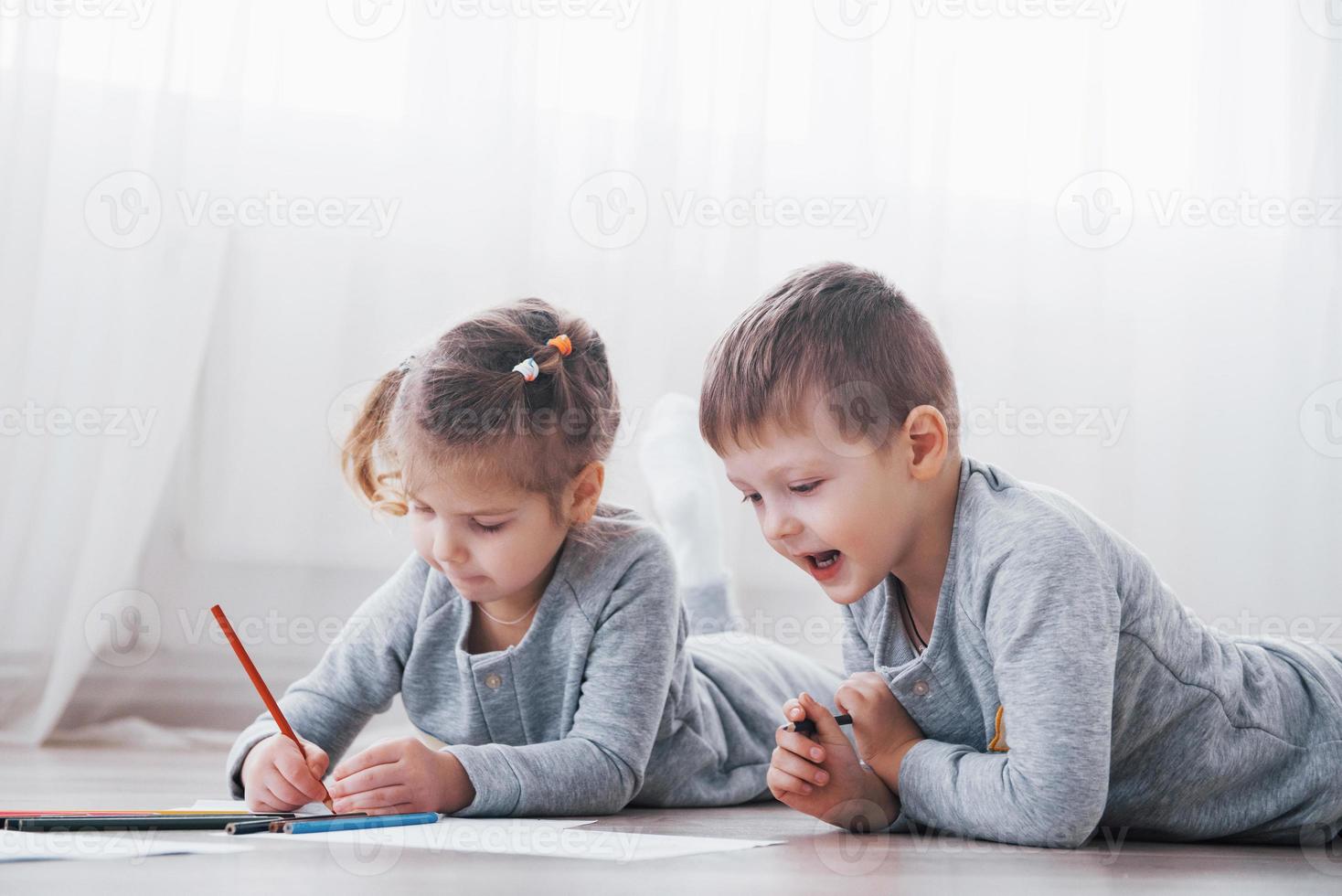 los niños se acuestan en el suelo en pijama y dibujan con lápices. lindo niño pintando con lápices foto