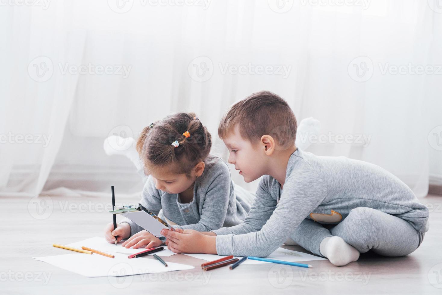 los niños se acuestan en el suelo en pijama y dibujan con lápices. lindo niño pintando con lápices foto