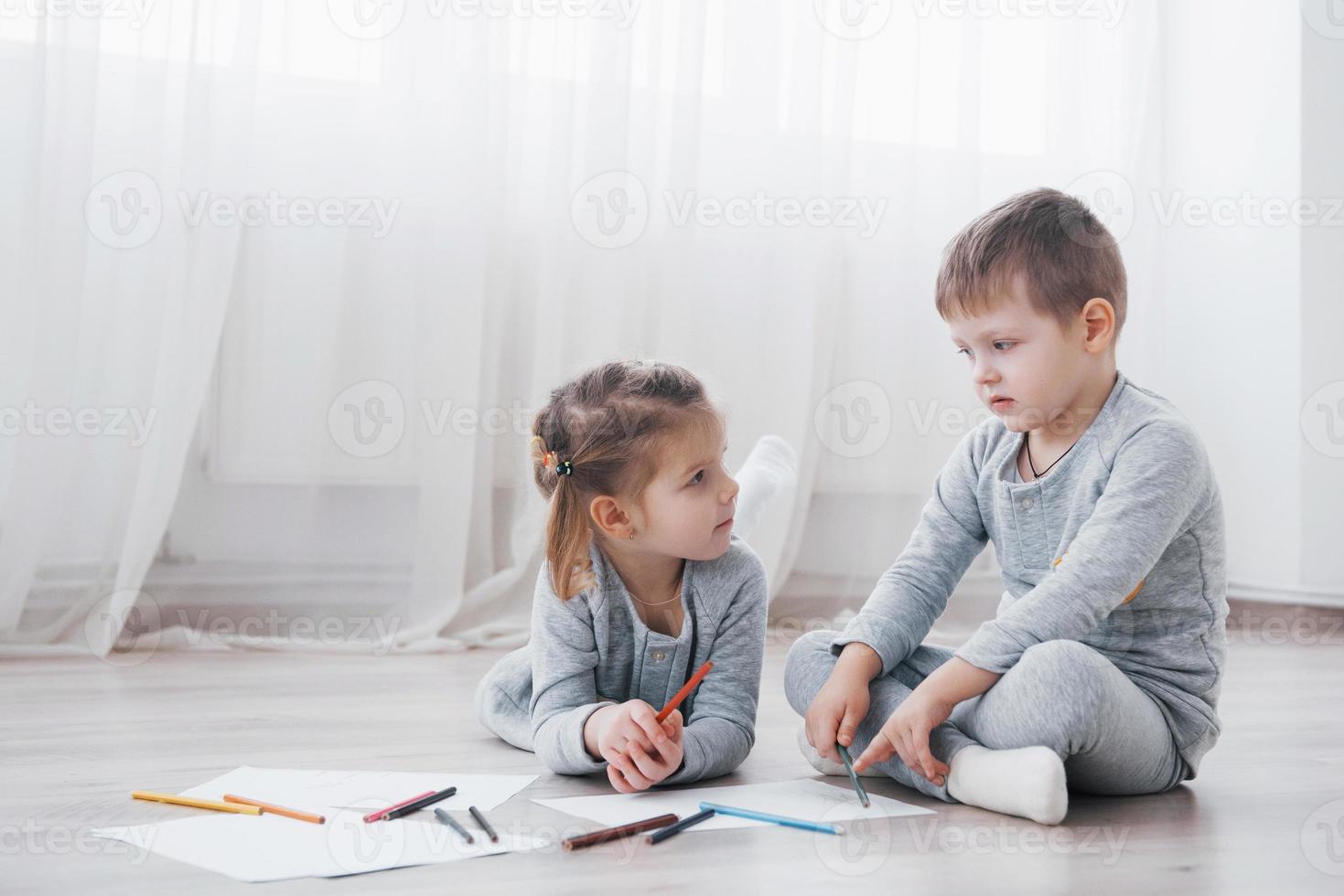 los niños se acuestan en el suelo en pijama y dibujan con lápices. lindo niño pintando con lápices foto