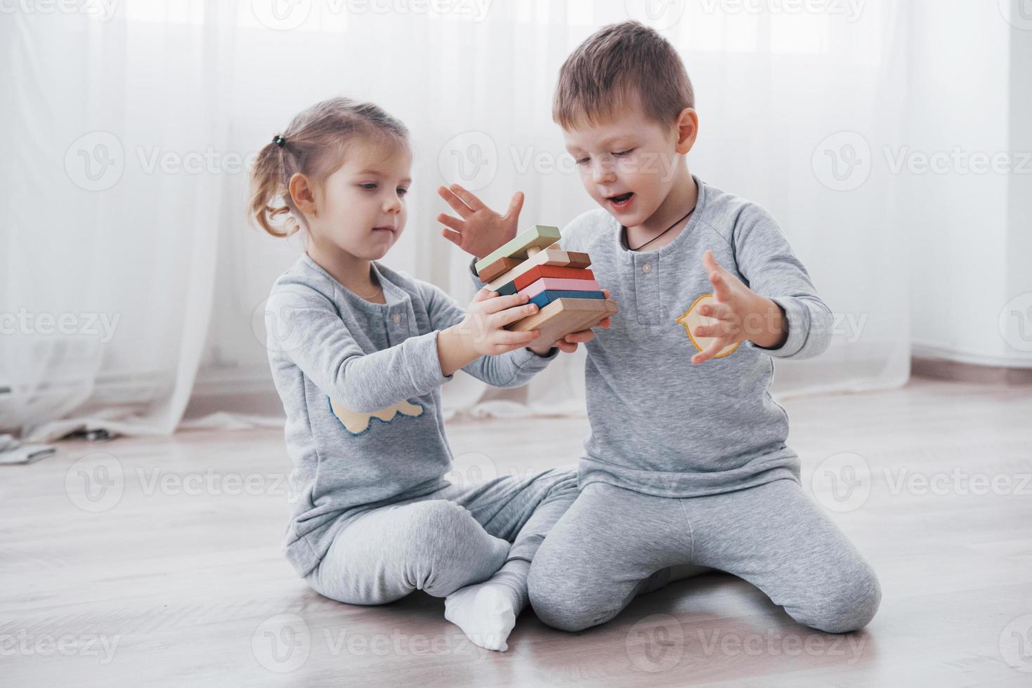 Los niños juegan con un diseñador de juguetes en el piso de la habitación de los niños. dos niños jugando con bloques de colores. juegos educativos de jardín de infantes foto