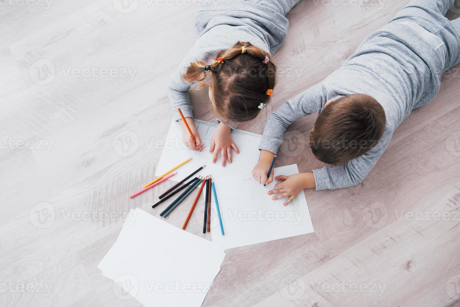 Children lie on the floor in pajamas and draw with pencils. Cute child painting by pencils. photo